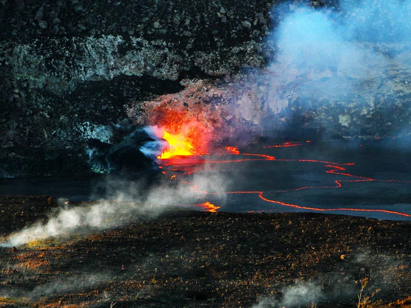 Bright orange volcanic lava and smoke rising from Hawaiin volcano covered with black lava
