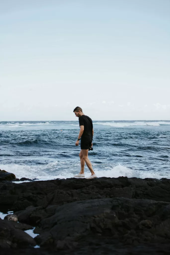 Man walking on a rocky outcropping at the Punalu'u Black Sand Beach located on the drive from Kona to Volcano.