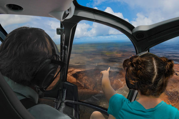 A little girl in a helicopter volcano tour points to Halemaʻumaʻu Crater as the pilot looks on.