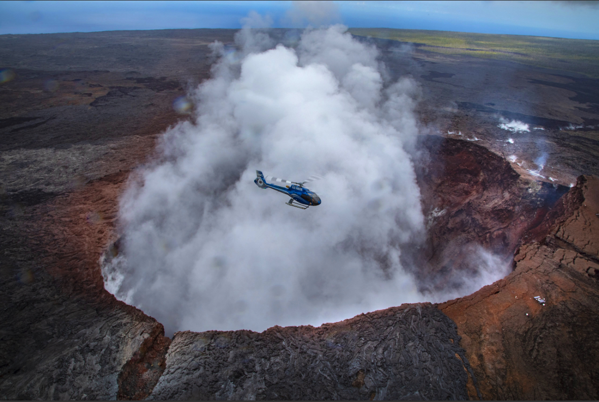 Helicopter circling over volcano crater filled with smoke