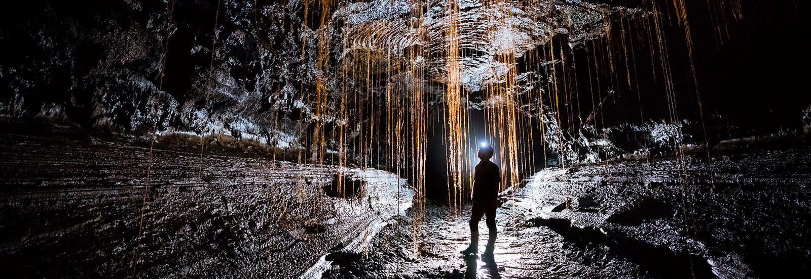 Man exploring inside of inactive volcano surrounded by hardened black lava and wearing headlamp