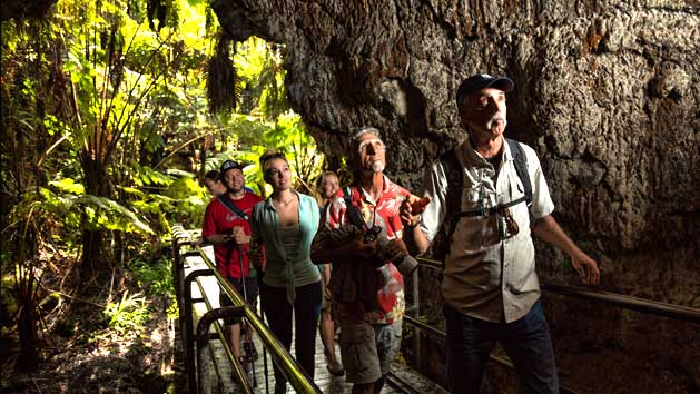 Tourists at entrance of lava tube surrounded by lush greenery on a Kilauea tour from Kona called Elite Volcano Hike