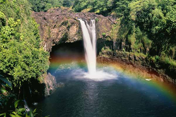 Waterfall surrounded by lush greenery with a rainbow right over the water in Oahu, Hawaii